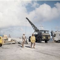 Ouvriers polynésiens devant un camion grue du génie, au pied d'un bâtiment de la Marine nationale au port de Moruroa.