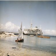 Au port de Moruroa, deux personnels naviguent près du rivage en dériveur, non loin du bâtiment-base Maurienne (A637) et du bâtiment-citerne à eau Liamone ex-Arrosoir (A750) à quai.