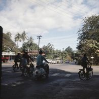 Automobiles et deux-roues circulant dans une rue de Papeete (cours de l'Union sacrée et avenue du Prince Hinoï ?), à proximité d'une station service.