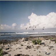 Vol en formation à basse altitude au-dessus du rivage de cinq hélicoptères Alouette II, probablement du groupe aérien mixte 82 (GAM 82), et un Alouette III à Moruroa.