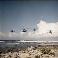 Vol en formation à basse altitude au-dessus du rivage de quatre hélicoptères Alouette II, probablement du groupe aérien mixte 82 (GAM 82), à Moruroa.