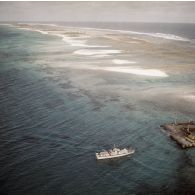 Vue aérienne du ponton du motus Faucon sur l'atoll de Moruroa, avec le côté lagon et le côté océan. Un canot arrive au débarcadère.