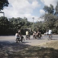 Habitants à solex et à vélo circulant dans une rue de Papeete.