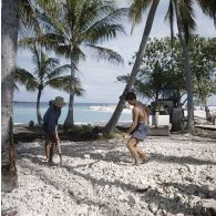 Deux ouvriers aplanissent  un terrain caillouteux à la pelle, non loin d'un engin rouleau compresseur sur la base avancée d'Hao.