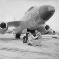 Au pied d'un avion Vautour de retour de mission, deux membres de l'équipe de décontamination en tenue de protection mesurent à l'aide d'un détecteur la radioactivité de l'aéronef, sur l'atoll d'Hao.