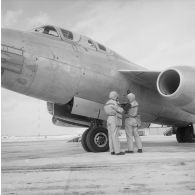 Au pied d'un avion Vautour de retour de mission, deux membres de l'équipe de décontamination en tenue de protection mesurent à l'aide d'un détecteur la radioactivité de l'aéronef, sur l'atoll d'Hao.