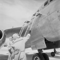 Deux mécaniciens en tenue de protection installent les échelles pour les pilotes d'un avion Vautour sur l'atoll d'Hao. Décontamination de l’aéronef de retour de mission.