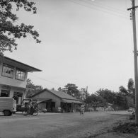 Commerces et passage d'un femme en solex sur une route à Tahiti.