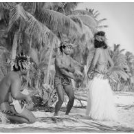 Un couple de danseurs, coiffés d'une couronne fleurie, fait une démonstration de danse du Tamoure, accompagnés par un guitariste sur une plage de l'atoll d'Hao.