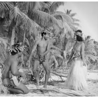 Un couple de danseurs, coiffés d'une couronne fleurie, fait une démonstration de danse du Tamoure, accompagnés par un guitariste sur une plage de l'atoll d'Hao.