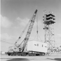 Levage d'un shelter au-dessus d'une remorque par un camion grue P&H sur le site du poste de commande de tir (PCT) Anémone au pied d'une antenne de transmission à Moruroa.