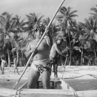 Deux jeunes hommes s'éloignent du rivage et de la plage sur une pirogue à balancier à Hao.