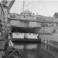 Deux barges transportant des shelters entrent dans le radier du transport de chalands de débarquement (TCD) Ouragan sous le regard de l'équipage dans le lagon de l'atoll de Moruroa.