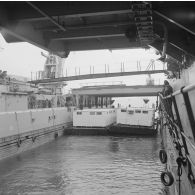 Deux barges transportant des shelters entrent dans le radier du transport de chalands de débarquement (TCD) Ouragan sous le regard de l'équipage dans le lagon de l'atoll de Moruroa.