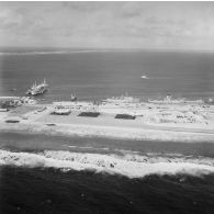 Vue aérienne de la zone aéroportuaire de l'atoll de Moruroa. Avions Breguet Deux Ponts au parking de l'aéroport, et en arrière-plan, le navire-atelier de mécanique et charpentage Garonne (A617), le bâtiment-base (BB) Maurienne (A637), le bâtiment de soutien santé (BSS) Rance (A618) et le bâtiment de soutien logistique (BSL) Tarn (A771) à quai au port.