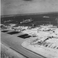 Vue aérienne de la zone aéro-portuaire de l'atoll de Moruroa. Avions Breguet Deux Ponts au parking de l'aéroport, et à quai, les bâtiments-bases (BB) Maurienne (A637) et Médoc (A612), le bâtiment de soutien santé (BSS) Rance (A618). Un bâtiment de la force Alpha au mouillage dans le lagon.