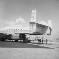 Déchargement d'un avion Breguet Deux Ponts au parking de l'aéroport de Moruroa à l'aide d'un engin de manutention Armat. En arrière-plan, le bâtiment-base (BB) Maurienne (A637) à quai au port.