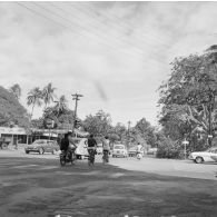 Circulation des deux-roues, vélos et solex, et des voitures dans une rue qui croise le cours de l'Union sacrée, à Papeete, non loin d'une station service.