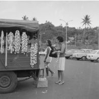 Sur un parking de l'aéroport de Faa'a à Papeete, une femme tahitienne achète des colliers de coquillage à un étal sur une camionnette.