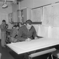 Le bureau météo à bord du croiseur de commandement De Grasse. Portrait d'un technicien dessinant sur une carte installée à une table à dessin.