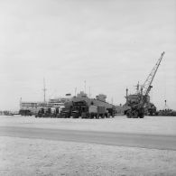 Au port de Moruroa devant le bâtiment-base (BB) Maurienne (A637), alignement d'engins de manutention Manitou sur un quai et déchargement d'un transport de chalands de débarquement (TCD).