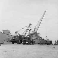 Au port de Moruroa sur un quai, déchargement de camions devant un transport de chalands de débarquement (TCD).