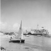 Deux militaires mettent un petit dériveur à l'eau dans le port de Moruroa. En arrière-plan, le bâtiment-base Maurienne (A637), le bâtiment de soutien logistique (BSL) Garonne (A617) et le transport ravitailleur d'eau douce Liamone (A750).