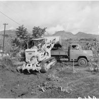 Engin du génie Traxcavator CAT 955 H déchargeant de la terre dans un camion benne pour le terrassement. Peut-être la construction du camp d'Arue, 1964.