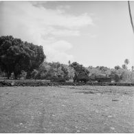 Ouvriers tahitiens travaillant au terrassement ou à la construction de route avec tractopelle et camions-bennes, camp d'Arue (?), vers 1963-1964.