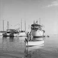 La goélette Taporo dans le port de Papeete, au premier plan des enfants jouant sur une barque, 1964.