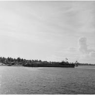 Vue depuis l'eau du rivage et du camp militaire. Bâtiments à quai (LST L9069 ?). Peut-être sur l'atoll de Moruroa.