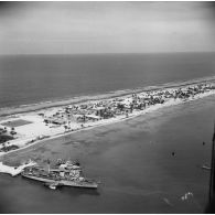 Vue aérienne d'installations sur l'atoll. Aviso-colonial Francis Garnier F730 et navire-atelier annexe L9099 (ancien landing craft tank ou LCT) à quai. Peut-être l'atoll de Moruroa.