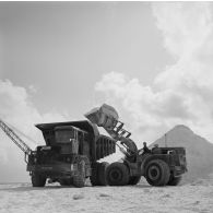 Camion à benne Willeme et engin tractopelle du génie Caterpillar pour le terrassement. Peut-être sur l'atoll de Moruroa.