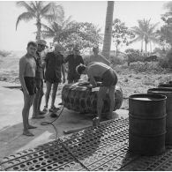 Militaires s'affairant à la réparation d'une roue d'engin du génie. Peut-être sur l'atoll de Moruroa.