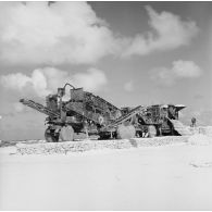 Engin du génie (extraction ou concassage de minéraux) sur un chantier de construction avec convoyeur à bande. Peut-être sur l'atoll de Moruroa.