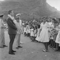 Accueil d'Alain Peyrefitte, ministre de l'Information, collier de fleurs autour du cou, et du contre-amiral François Picard-Destelan, commandant les forces armées françaises dans le Pacifique, par une jeune fille polynésienne pour une cérémonie. A Vaitape (Bora-Bora).