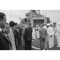 Le général Charles De Gaulle, président de la République, salue des personnels civils à bord du croiseur De Grasse, suivi par Pierre Messmer, ministre des Armées, et Alain Peyrefitte, ministre de la Recherche scientifique et des Questions atomiques et spatiales.