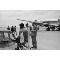 Accueil du général Charles De Gaulle, président de la République, par le vice-amiral Jean Lorain, commandement du groupe opérationnel des expérimentations nucléaires (GOEN), à l'aéroport de Moruroa. Au premier plan, le chauffeur et la voiture officielle Peugeot 403 avec le drapeau aux initiales du président.