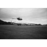 Atterrissage d'un hélicoptère Alouette 2 devant cinq avions Breguet Deux-Ponts stationnés sur la partie militaire (motu Tahiri) de l'aéroport de Faa'a, vers 1964-1965.