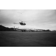 Atterrissage d'un hélicoptère Alouette 2 devant cinq avions de transport Breguet Deux-Ponts stationnés sur la partie militaire (motu Tahiri) de l'aéroport de Faa'a, vers 1964-1965.