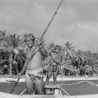 Deux jeunes hommes s'éloignent du rivage et de la plage sur une pirogue à balancier à Hao.