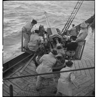 Chargement et pointage d'un canon de 75 mm à bord d'un chalutier armé naviguant en convoi.