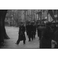 Un vice-amiral d'escadre, accompagné d'officiers de Marine, passe en revue des unités de l'armée de Terre et de la Marine lors d'une prise d'armes.