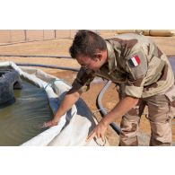 Le sergent-chef Thomas du 19e régiment du génie (RG) prélève un échantillon d'eau dans un bac souple au point d'appui conjoint (PAC) d'Ayorou, au Niger.