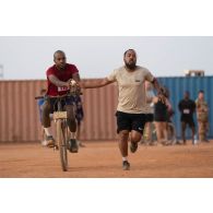 Un cycliste hydrate son binôme à pied pour un semi-marathon autour de la plateforme logistique de PK11, au Niger.