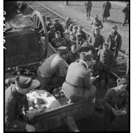 Des soldats perçoivent leur ration pour le repas le long d'une voie ferrée en gare de Trappes.