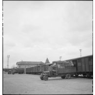 Plan général d'une opération de transbordement : des camions  garés prés des portes de wagons de marchandises sont chargés de produits alimentaires.