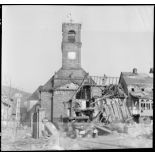 Un camion Dodge WC circule dans le village de Masevaux en ruine. A l'arrière plan, l'église Saint-Martin.
