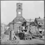 Un camion Dodge WC 62 circule dans le village de Masevaux en ruine. A l'arrière plan, l'église Saint-Martin.