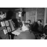 Des officiers de la Luftwaffe lors d'un repas, un sous-officier joue de l’accordéon.